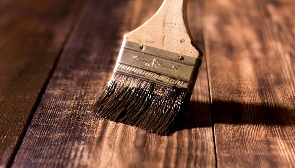 Brush applying rich stain to a wood deck